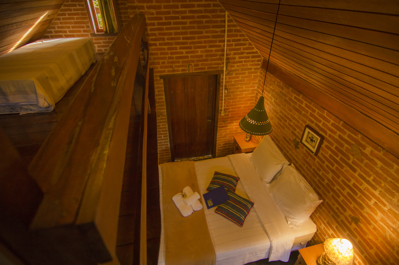 Cama vista do mezanino, com a porta de madeira e as luminárias