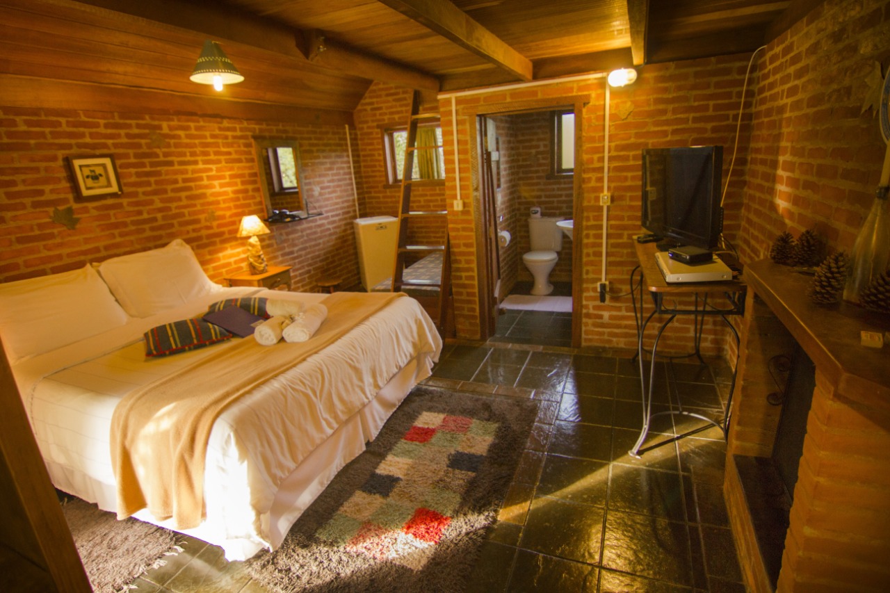 Quarto do Chalé Araucária, com a cama, a escada do mezanino e o banheiro ao fundo
