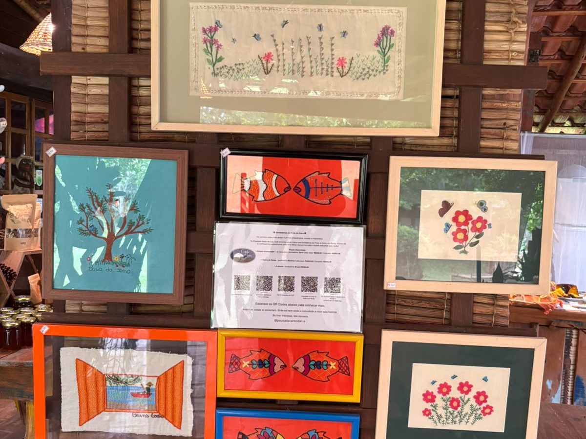 Parede de treliça com quadros bordados à mão: flores, peixes coloridos, uma árvore e uma janela com barco