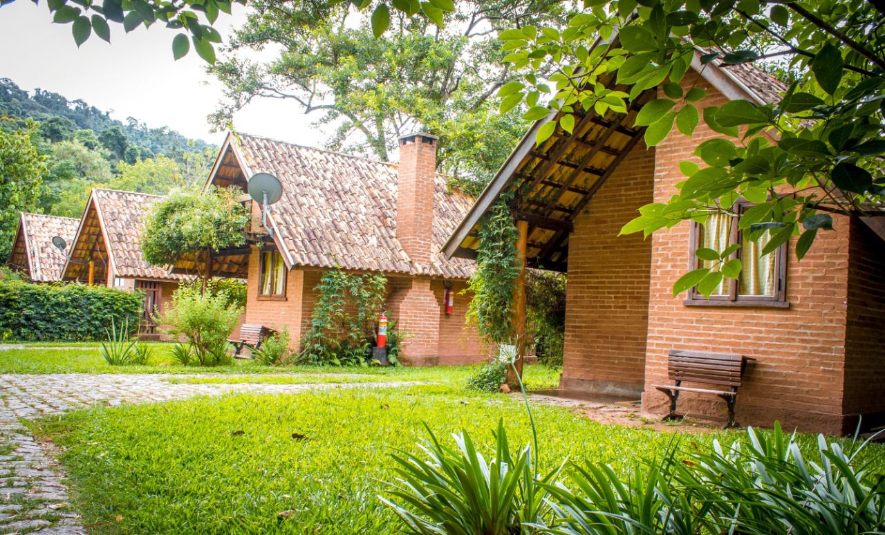 Chalés de tijolo da Pousada Canto da Lua entre o jardim e as árvores da Mantiqueira