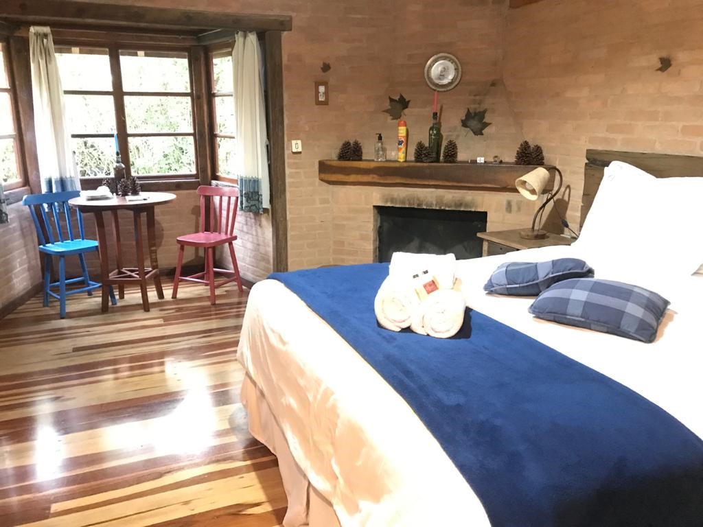 Cama com manta azul e a mesa junto à janela ao fundo