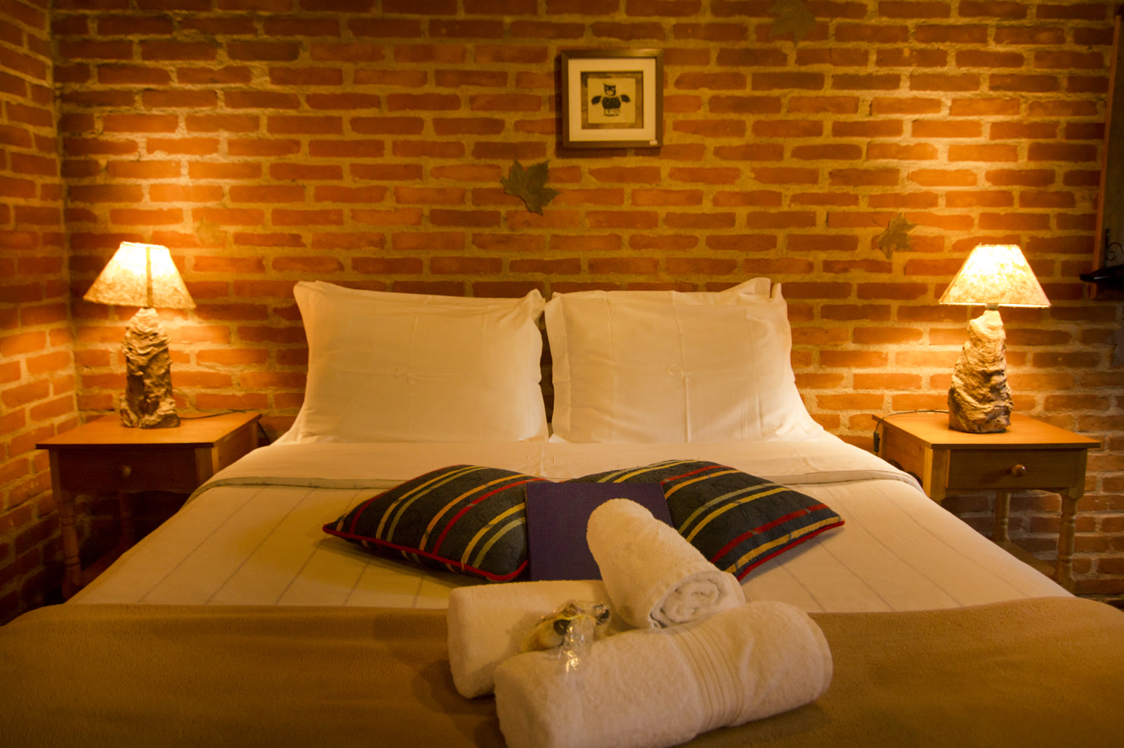 Cama do Chalé Ipê entre dois abajures acesos, com almofadas listradas e toalhas dobradas