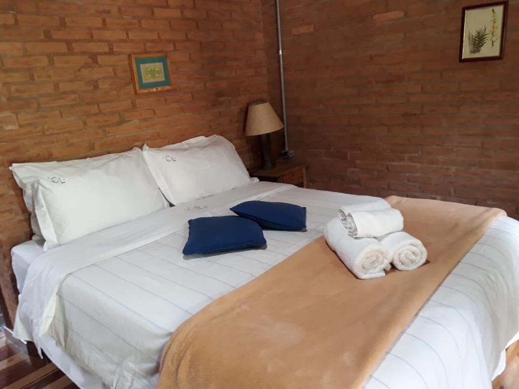 Cama com almofadas azuis, manta bege e toalhas dobradas