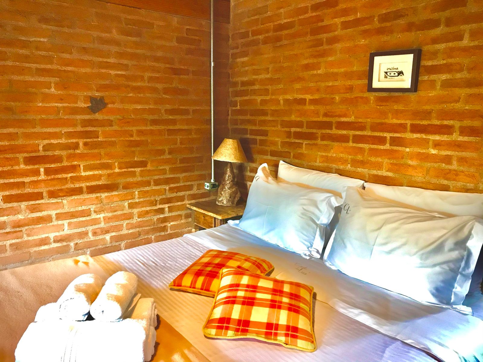 Cama do Manacá com almofadas xadrez laranja e toalhas dobradas