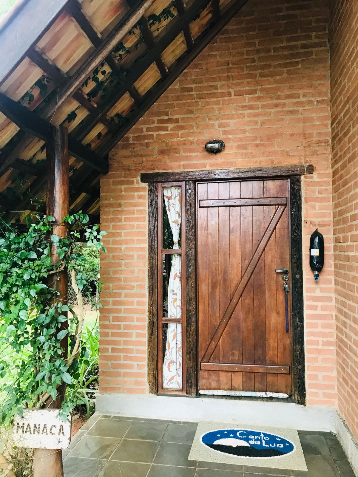 Porta de madeira do Chalé Manacá, com a placa e o tapete Canto da Lua