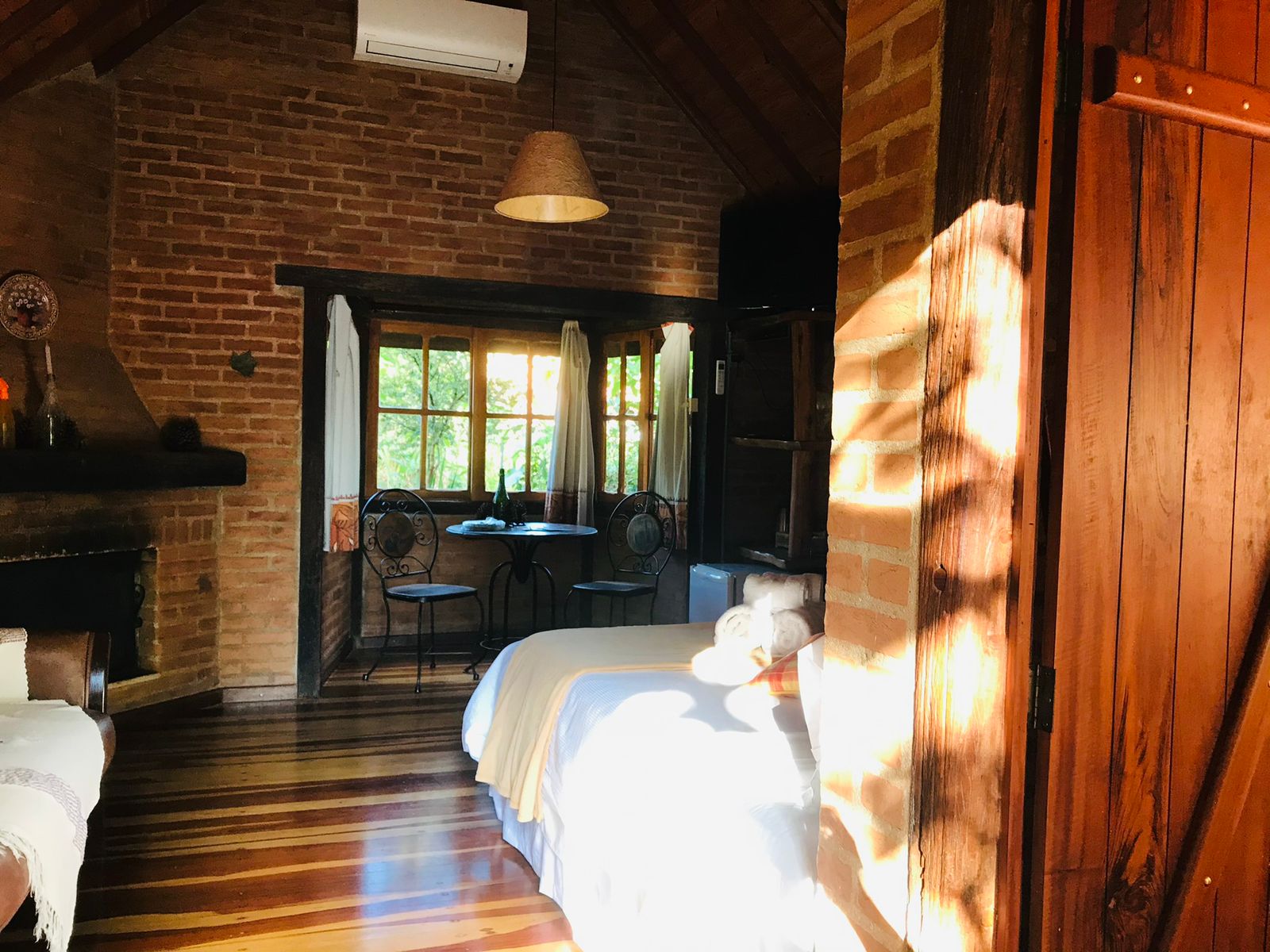 Sol entrando pela porta do chalé, com a lareira e a mesa ao fundo