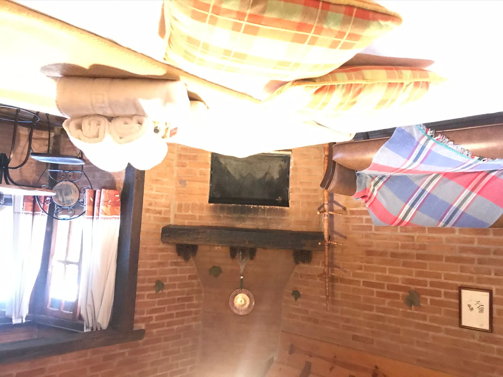 Almofadas xadrez sobre a cama, com o sofá e a lareira ao fundo