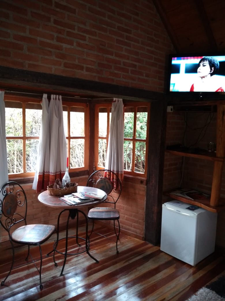 Mesa de ferro e cadeiras junto à janela, com TV e frigobar