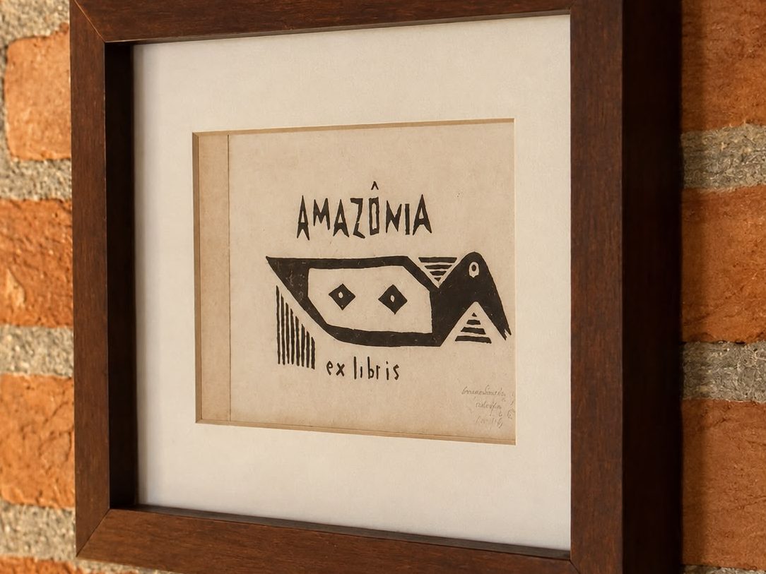 Xilogravura de Marlene Crespo emoldurada na parede de tijolos: um pássaro estilizado entre as palavras Amazônia e ex libris