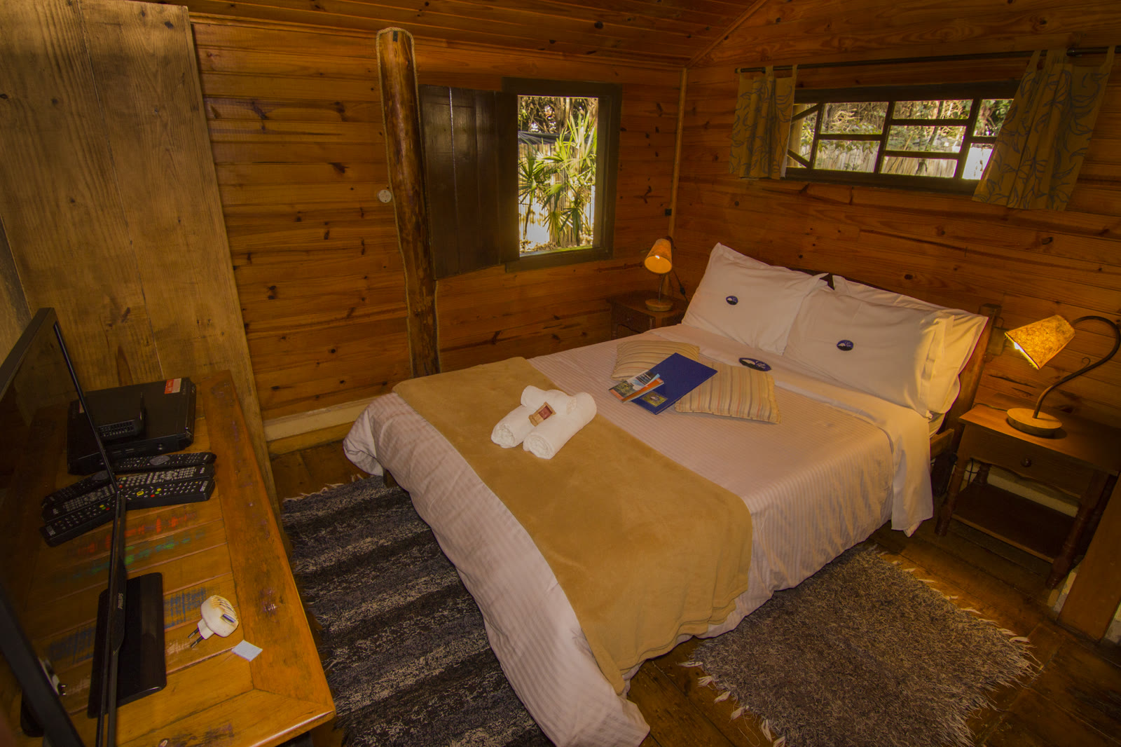 Quarto de madeira do Paineiras, com a cama, os abajures e a janela para a mata