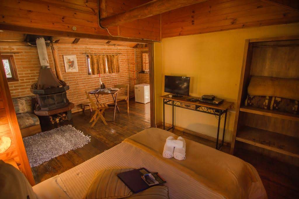 Vista da cama para a sala do Paineiras, com a lareira, a mesa e a TV