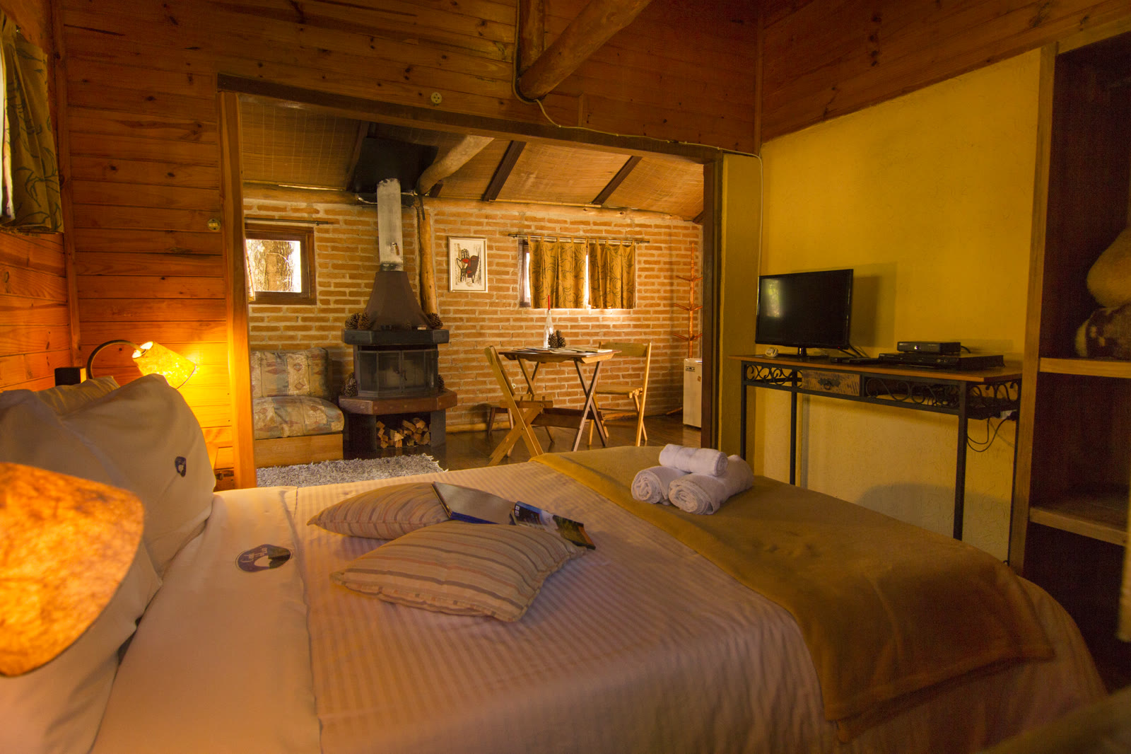 Cama com almofadas e toalhas, e a lareira e a mesa ao fundo