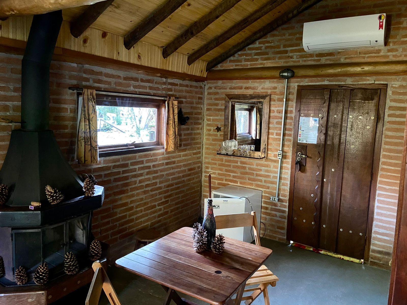 Sala com o fogão a lenha, a mesa dobrável e a porta de madeira