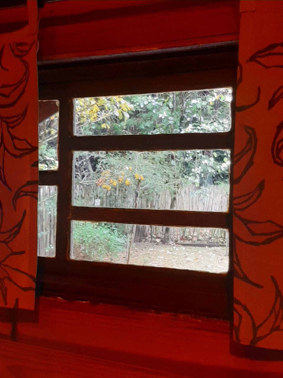 Janela com cortina vermelha e vista para a mata