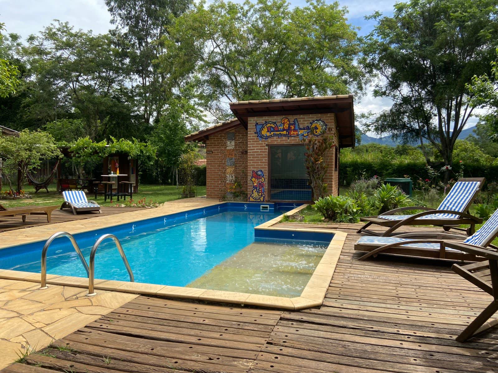 Piscina com deck de madeira, espreguiçadeiras e a sauna de vidro ao fundo