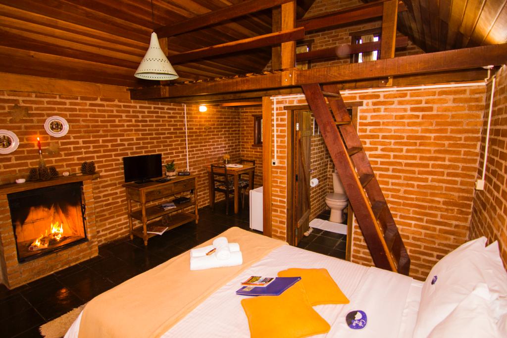 Quarto do Chalé Platanus com a lareira acesa, a cama e a escada para o mezanino