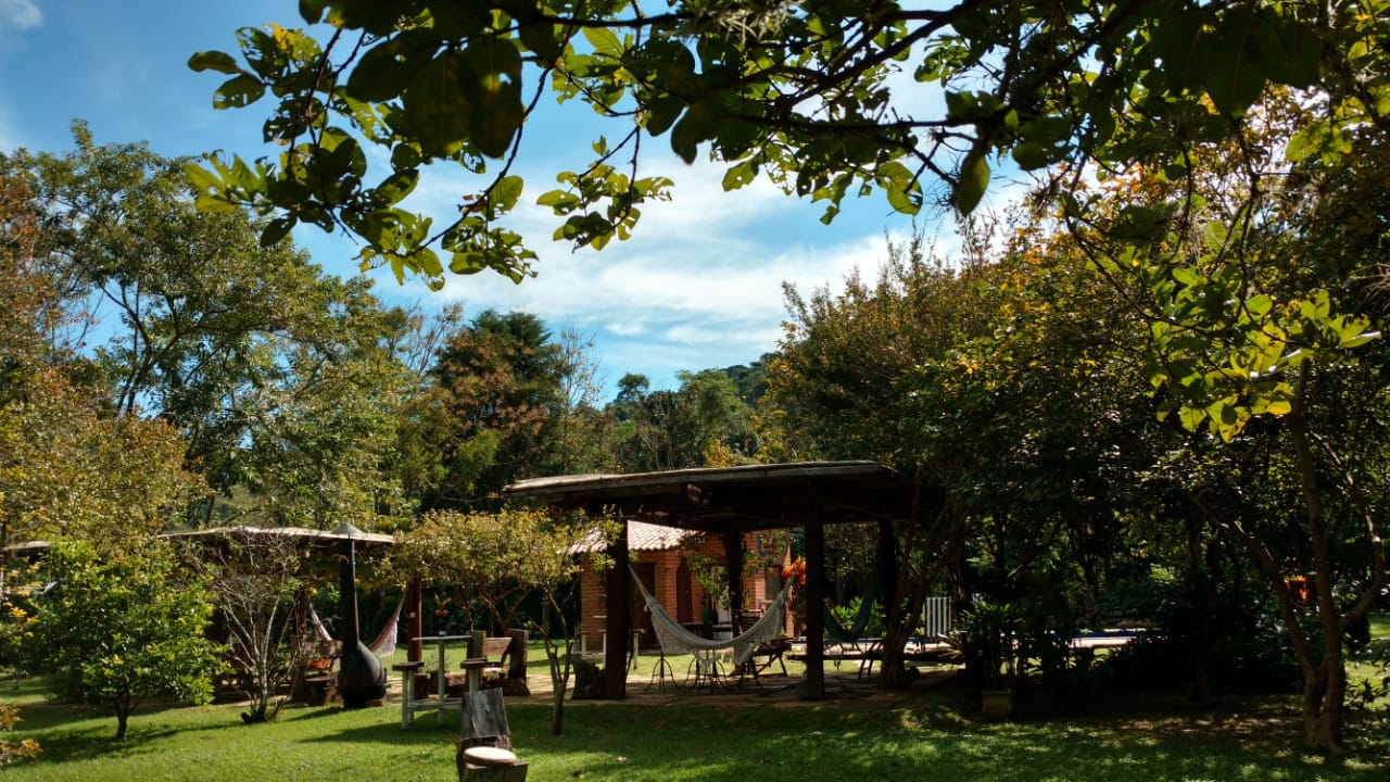 Redário e piscina da pousada sob as árvores num dia de sol